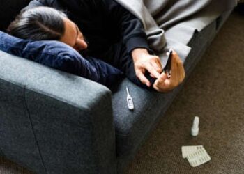 El hombre está en sofá enfermo de termómetro, teléfono y pllls