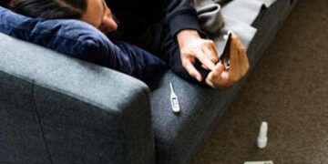 El hombre está en sofá enfermo de termómetro, teléfono y pllls