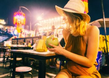 Mujer con sombrero de paja bebiendo un cóctel en un mercado nocturno.