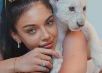 Mujer con un cachorro de león blanco en el hombro.