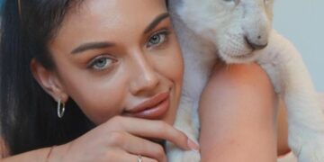 Mujer con un cachorro de león blanco en el hombro.