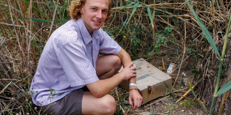 Hombre agachado junto a una trampa de serpiente en un humedal.