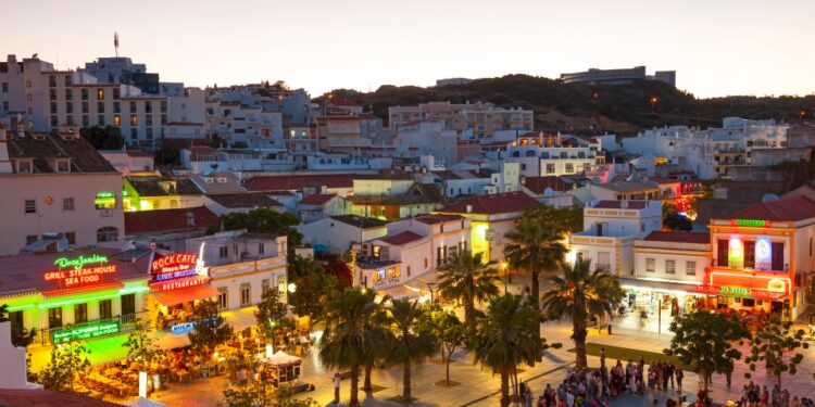Albufeira, Portugal Town Square al anochecer, con personas reunidas e iluminadas edificios.