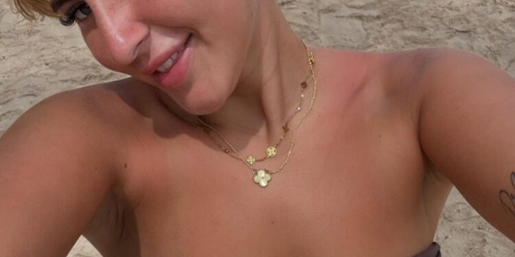 Mujer en una playa con una tapa de bikini marrón y collares de oro.