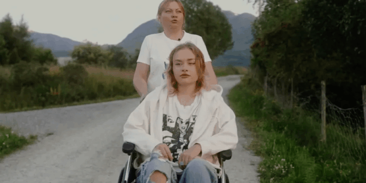 Mujer empujando a una mujer joven en una silla de ruedas por un camino rural.