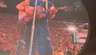 Chris Martin tocando la guitarra en una pantalla grande en un concierto.