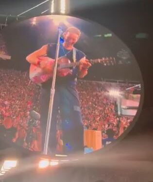 Chris Martin tocando la guitarra en una pantalla grande en un concierto.