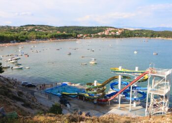 Vista aérea de una playa con toboganes de agua y muchos barcos.