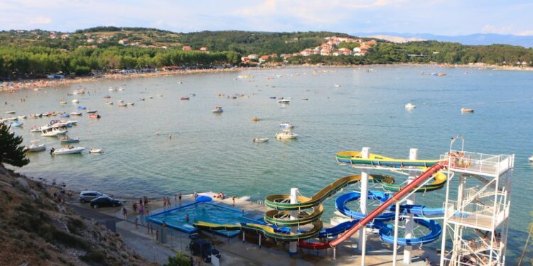 Vista aérea de una playa con toboganes de agua y muchos barcos.