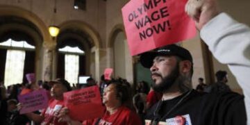 Los residentes de Los Ángeles tienen letreros leyendo "Salario olímpico ahora" Durante un rally interior