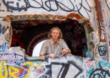 Un joven mira desde un agujero en una pared cubierta de graffiti.