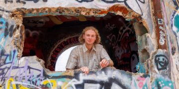 Un joven mira desde un agujero en una pared cubierta de graffiti.