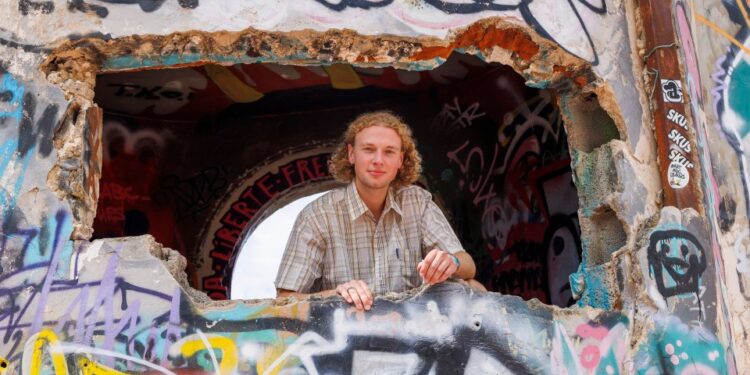 Un joven mira desde un agujero en una pared cubierta de graffiti.