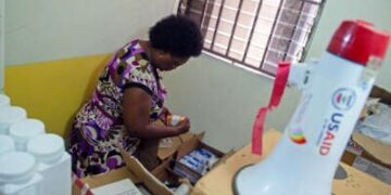 Una enfermera busca en cajas como un megáfono con un "USAID" El logotipo en él se ve en primer plano