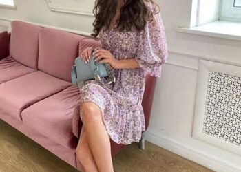 Mujer con vestido floral sentado en un sofá rosa.