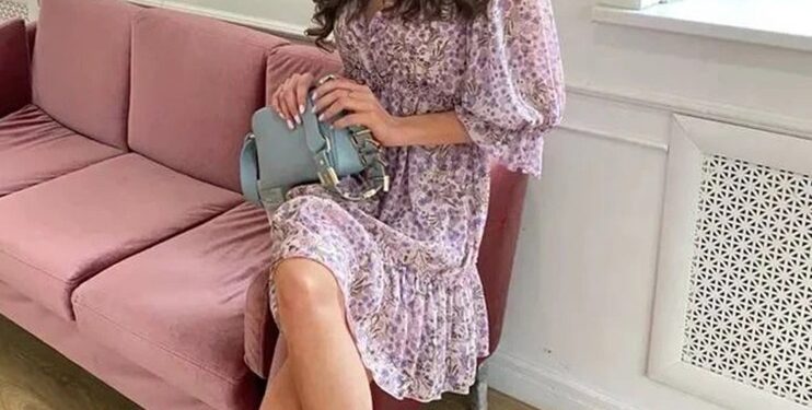 Mujer con vestido floral sentado en un sofá rosa.