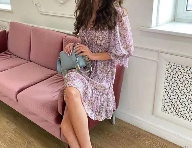 Mujer con vestido floral sentado en un sofá rosa.