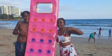 Dos niños en una playa con una balsa inflable rosa.