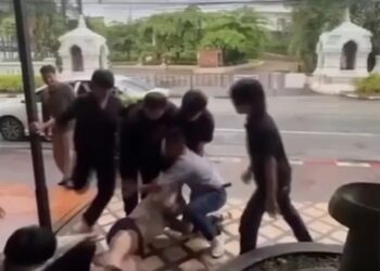 Un hombre siendo restringido y pateado por varios hombres fuera de un bar.