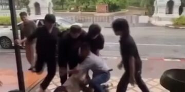 Un hombre siendo restringido y pateado por varios hombres fuera de un bar.