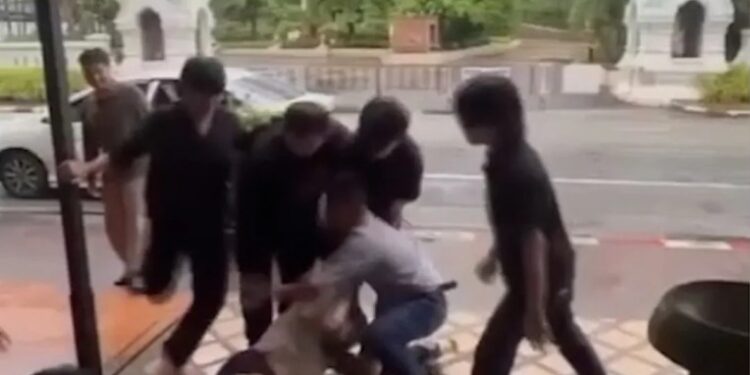 Un hombre siendo restringido y pateado por varios hombres fuera de un bar.