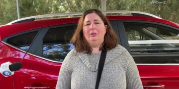 Mujer siendo entrevistada frente a un coche rojo.