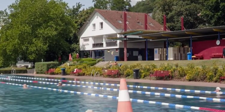 Piscina al aire libre con nadadores y un edificio en el fondo.