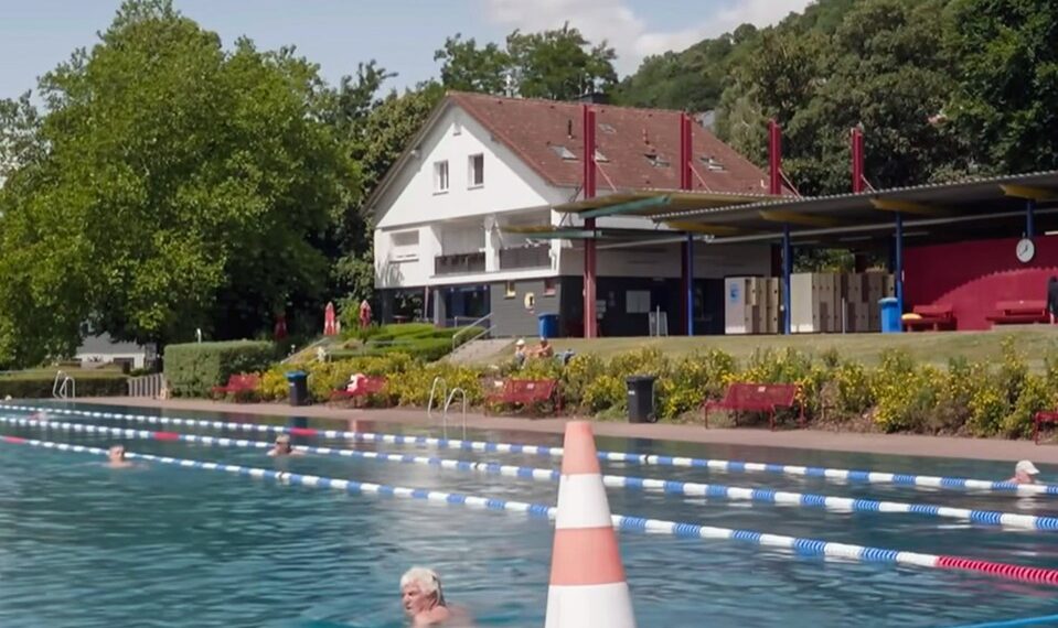 Piscina al aire libre con nadadores y un edificio en el fondo.