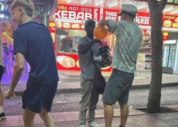 Tres personas en una calle por la noche, uno sostiene un globo naranja.