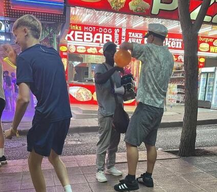 Tres personas en una calle por la noche, uno sostiene un globo naranja.