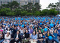 Las personas que sostienen palos de luz y globos azules animan durante un rally político