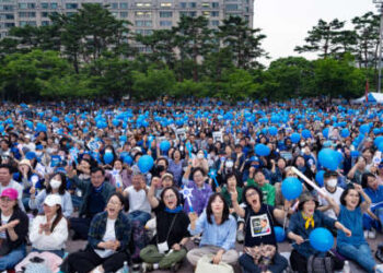 Las personas que sostienen palos de luz y globos azules animan durante un rally político