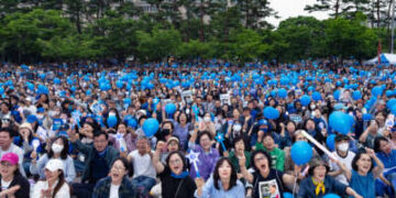 Las personas que sostienen palos de luz y globos azules animan durante un rally político