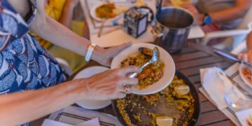 Una persona se sirve paella en un restaurante al aire libre.