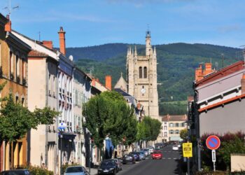 Escena callejera en Ambert, Francia, que muestra edificios, autos y una torre de la iglesia en el fondo.