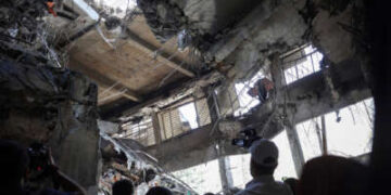 La gente mira a un agujero atravesado por una prisión por una bomba.