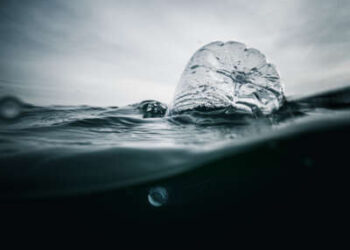 Botella de plástico que se balancea en el océano, nuestra vista parcialmente sumergida en la oscuridad