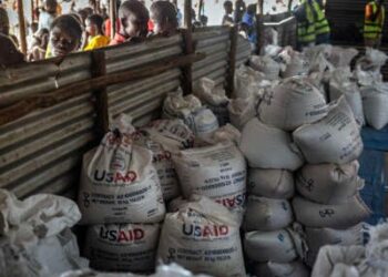 Los refugiados congoleños miran a través de una cerca de metal corrugada en los lotes finales de alimentos entregados por la ahora distraída Agencia de los Estados Unidos para el Desarrollo Internacional (USAID) en un área de almacenamiento y entrega de alimentos en el sitio de refugiados de Musenyi en Giharo, el 7 de mayo de 2025.