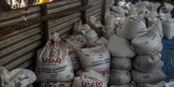 Los refugiados congoleños miran a través de una cerca de metal corrugada en los lotes finales de alimentos entregados por la ahora distraída Agencia de los Estados Unidos para el Desarrollo Internacional (USAID) en un área de almacenamiento y entrega de alimentos en el sitio de refugiados de Musenyi en Giharo, el 7 de mayo de 2025.