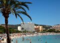 Playa llena de gente en Magaluf, Mallorca, con hoteles en el fondo.