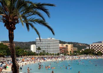 Playa llena de gente en Magaluf, Mallorca, con hoteles en el fondo.