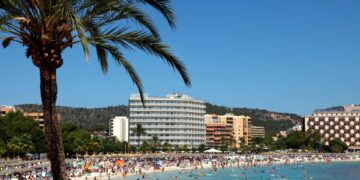 Playa llena de gente en Magaluf, Mallorca, con hoteles en el fondo.