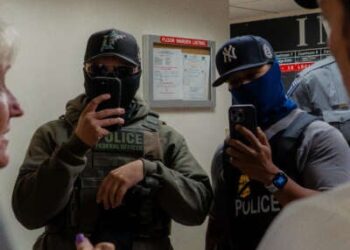 Dos agentes de ICE filman la prensa utilizando teléfonos inteligentes en el pasillo fuera del Tribunal de Inmigración en 26 Federal Plaza en Nueva York el 11 de julio de 2025.