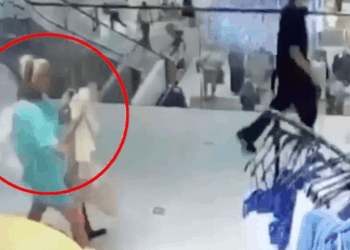 Captura de pantalla de una mujer con una camisa verde azulado que lleva algo en un centro comercial.