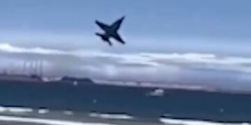 Avión a reacción volando sobre una playa llena de gente.