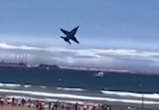 Avión a reacción volando sobre una playa llena de gente.