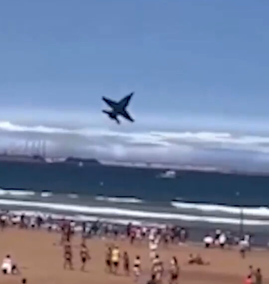 Avión a reacción volando sobre una playa llena de gente.