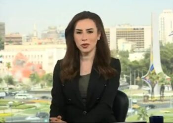 Ancre de noticias sentado frente a una ventana con vistas a una ciudad.