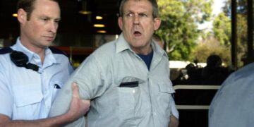 Un oficial de policía lleva a un sospechoso lejos de la Corte Suprema de Adelaide.