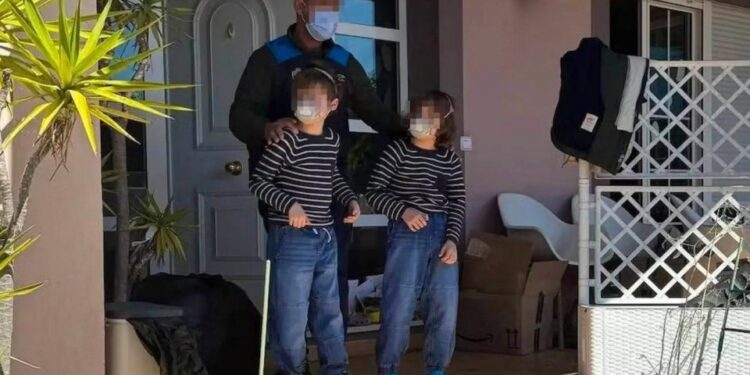 Oficial de policía con dos hijos fuera de una casa.